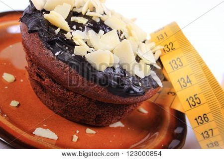 Homemade delicious fresh baked chocolate muffins with sliced almonds on brown plate and tape measure concept for slimming and dessert