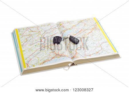 Open old road atlas and car keys lying on it on a light background