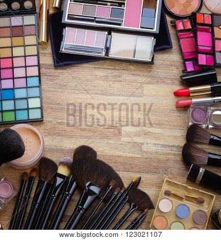 Frame of  brushes, lipsticks, maskara, eye shadows and  powder on wood, top view