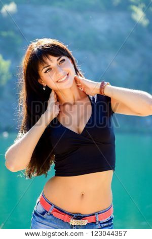 beautiful girl in a black top and denim shorts standing on the shore of a mountain lake