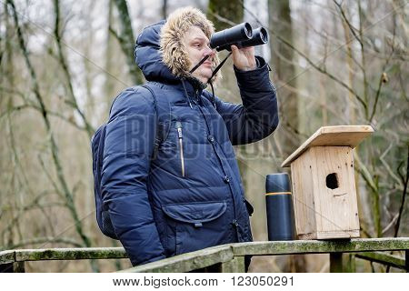 Ornithologist with binoculars and bird cage in the park on the bridge