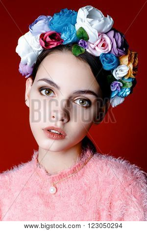 Beautiful model with a wreath of flowers on her head on red background. Beauty Woman face Portrait. Beautiful Spa model Girl with Perfect Fresh Clean Skin.