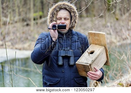 Ornithologist with camcorder and bird cage near river