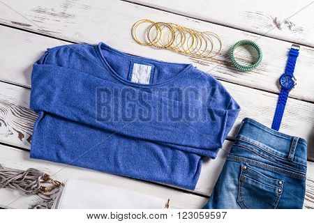 Female sweatshirt with blue jeans. Clothes and accessories on table. Tiny bracelets and spring clothes. Casual garments in clothes shop.