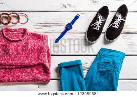 Pink sweatshirt with turquoise pants. Colorful outfit on white table. Bright clothing and black keds. Lady's outfit with fabric shoes.
