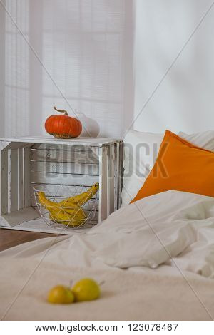 Close-up of apples and pumpkin in modern simple bedroom. Mattress on wooden floor as a bed