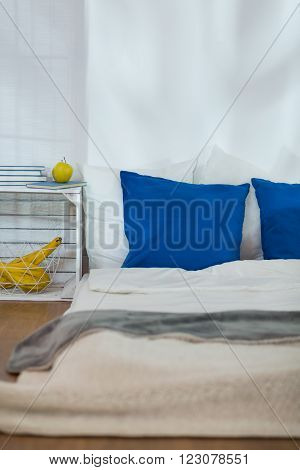 Modest simple bedroom with mattress on wooden floor and blue pillows. Wooden nightstand made of box