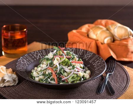 Pasta salad with vegetables served in a brown ceramic bowl set on a wooden table top.
