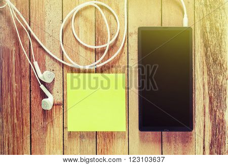 Closeup of black smartphone with headphones and sticky notes on wooden surface, Square image format Instant photo split toning color effect, Vintage style