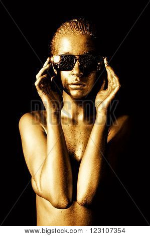 Beautiful naked young woman in gold with sunglasses.