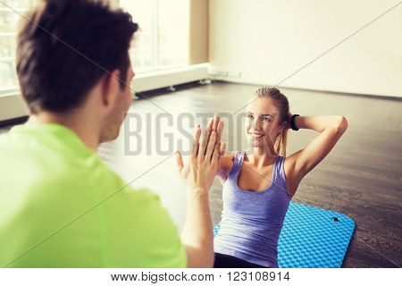 fitness, sport, training, teamwork and people concept - happy woman with personal trainer doing sit ups and high five gesture in gym