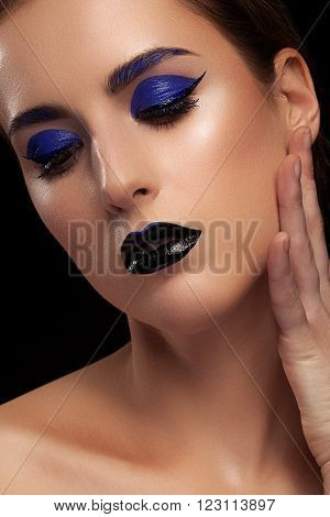 Womam with fashion blue make up on black background in studio shooting. Extravagant make up. Colorful art stage make up with black lips