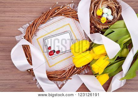 Easter with eggs in nest and yellow tulips over wooden table. Top view