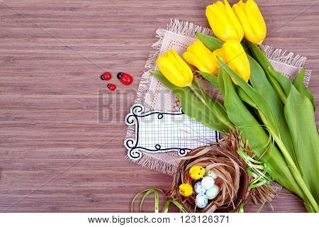 Easter with eggs in nest and yellow tulips over wooden table. Top view