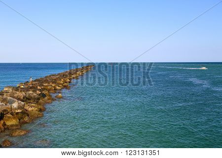 MIAMI BEACH, USA - MAY 9, 2015: Jetty at the entrance of the Port of Miami with an angler on it and a small yacht in the back.