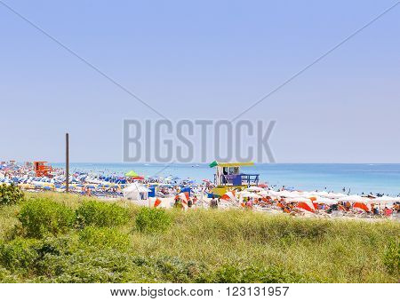 MIAMI BEACH, USA - MAY 9, 2015: Section of the beach with lifeguard stations and lots of colorful sunshades and beach chairs, in the front dunes with marram grass. People having fun in the sun.