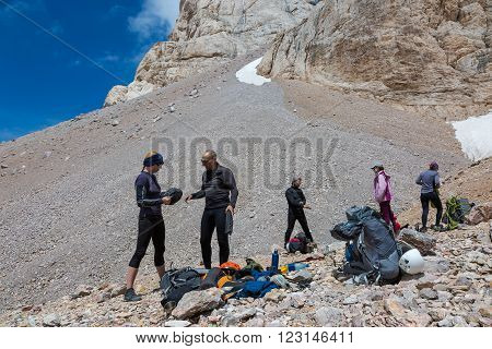 Group of Alpine Climbers Working on setting up Camping Tents with Many Gear Dropped Around and Rocky Mountain Moraine on Background