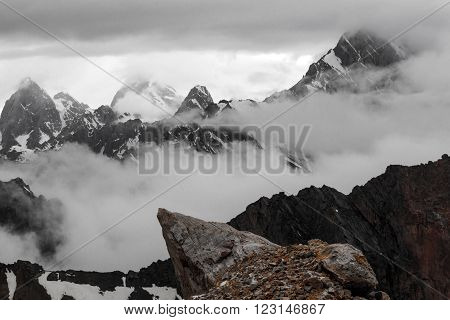 Landscape with Several Layers of Rocky Snowy Ridges mainly in Black and White Except Orange Rock on Foreground Overcast Clouds Sky