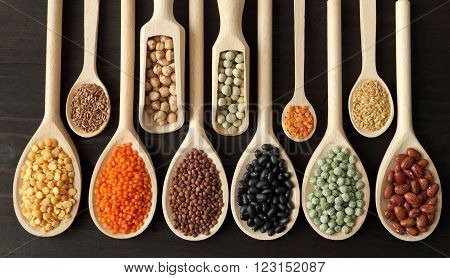Lentils peas and beans on wooden spoons.