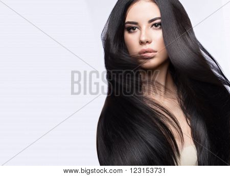 Beautiful brunette girl in move with a perfectly smooth hair, and classic make-up. Beauty face. Picture taken in the studio on a white background.