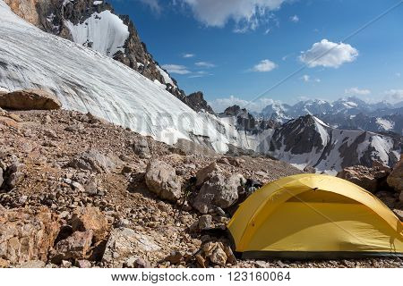 Mountain View with Ice Glacier and Peaks on Background and Small Single Alpine Yellow Tent located on Rocky Moraine on Foreground