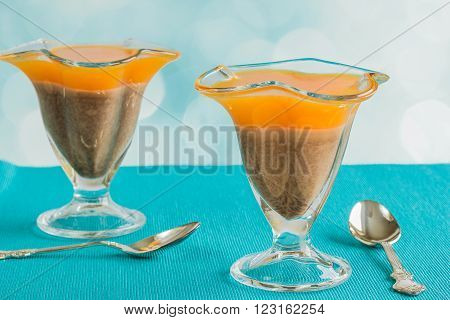 Two glasses with orange-chocolate jelly and two teaspoons on a blue napkin on blurred blue background