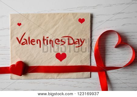 Blank present card with ribbon in form of heart on wooden background
