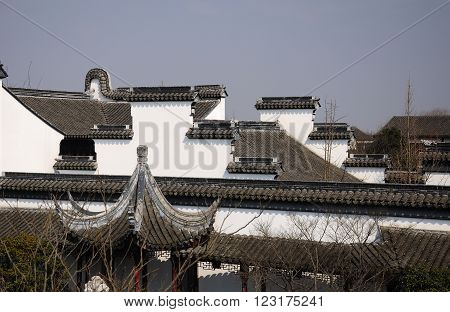 The white walls and rooftops of buildings at Li Yuan Garden in the water town of Zhaojialou in Shanghai China against a blue sky.