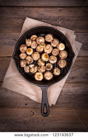 Garlic mushrooms cooked in a cast iron skillet, resting on greaseproof paper on old table. Overhead view with retro style processing.