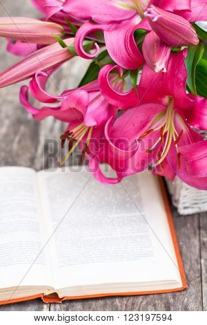 White basket with pink lily flowers bouquet and old book on rustic wooden table