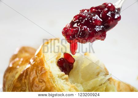 red cranberry jam on a spoon dripping on a fresh croissant, breackfast closeup shot with selected focus and narrow depth of field