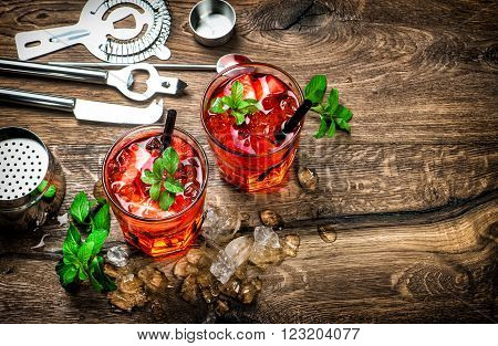 Red drink with ice mint leaves and strawberry. Cocktail campari aperol caipirinha mojito soda water. Dark toned picture
