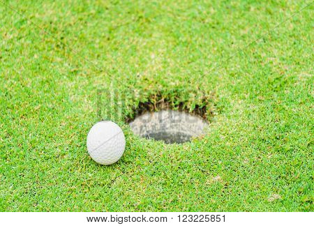 A golf ball near the lip of cup