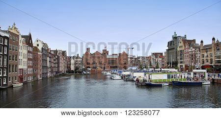 AMSTERDAM; THE NETHERLANDS - AUGUST 16; 2015: Beautiful views of the ancient buildings at the waterside, canal and boats, Damrak canal in Amsterdam, The Netherlands on August 16; 2015.