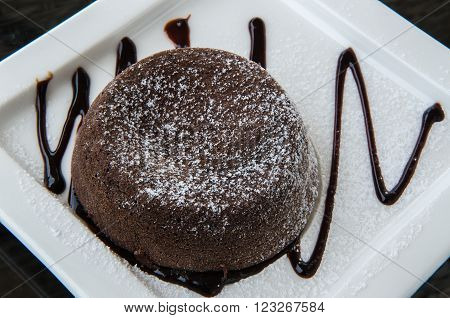 Chocolate lava cake topped with chocolate cream on a white plate.