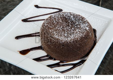 Chocolate lava cake topped with chocolate cream on a white plate.