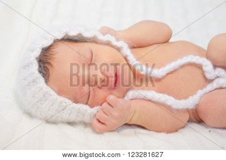 Sleeping smiling newborn baby in the white cap. Birth and a new life concept.