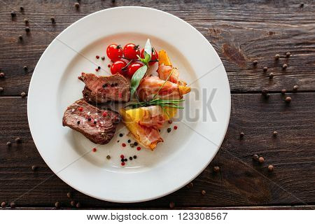 Medium rare pork steak with fresh vegetables. Food photography of pork steak with potatoes and tomatoes cherry. Tasty cook meat with vegetables on dark wooden background.