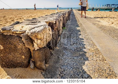 Waikiki, Honolulu, Hawaii, USA - December 13, 2015: Pathway to the jetty of the Atlantis Submarines Waikiki. On Waikiki Beach, near Fort DeRussy Broadwalk. A stone wall can be seen holding up the beach sand.