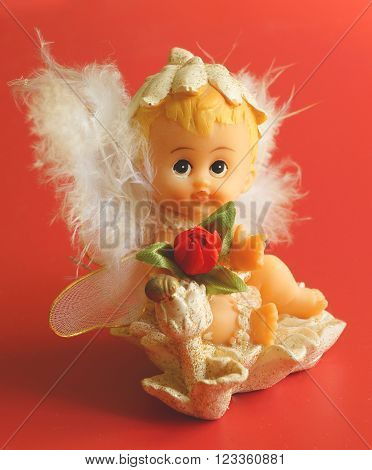 Little toy statue of fluff angel on red background