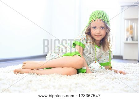 Cute girl wearing a green hat on a furry white carpet