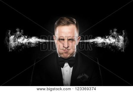 Stressful man with smoke or fume coming out from his ears on dark background.