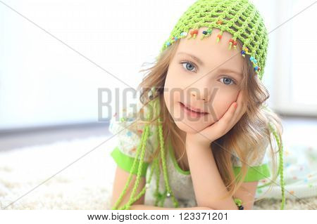 Cute girl wearing a green hat on a furry white carpet