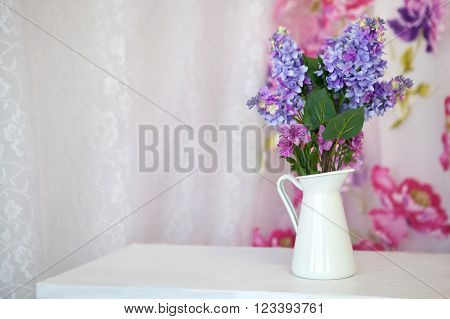 Bouquet branches purple lilac in a white vase on a table in the room