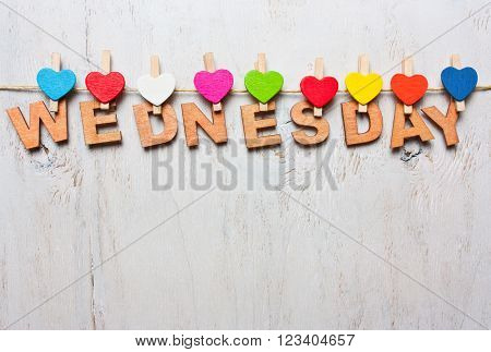 Wednesday word from wooden letters with colored clothespins on a white wooden background