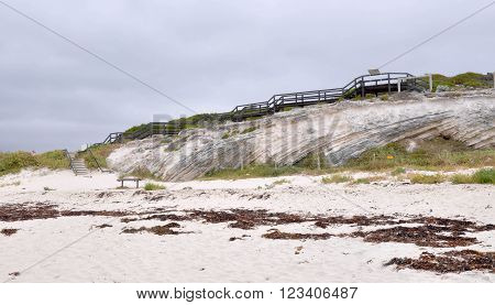 Coast line of Hamelin Bay, Western Australia with limestone cliffs, vegetated dunes and wooden boardwalk under dark stormy skies.