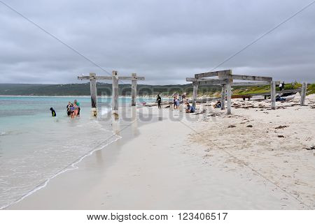 HAMELIN BAY,WA,AUSTRALIA-JANUARY 17,2016: People petting wild stingrays and jetty ruins on the beach under stormy skies in Hamelin Bay, Western Australia.