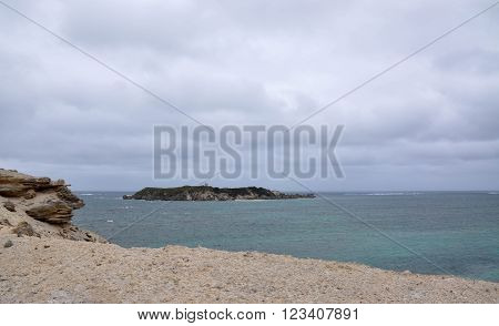 Turquoise Indian Ocean seascape with Hamelin Island view from the Hamelin Bay beach under dark, stormy skies in Western Australia.