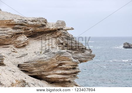 Layered limestone cliffs at White Cliff Point with Indian Ocean waters on a stormy day in Hamelin Bay, Western Australia.