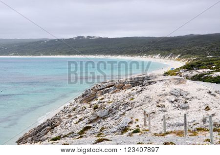 View over Hamelin Bay from the limestone bluff at White Cliff Point with turquoise Indian Ocean waters and vegetated dunes  under dark, stormy skies in Western Australia.